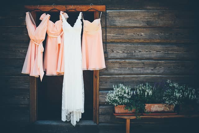 a wedding dress hanging alongside bridesmaid dresses on a wooden background