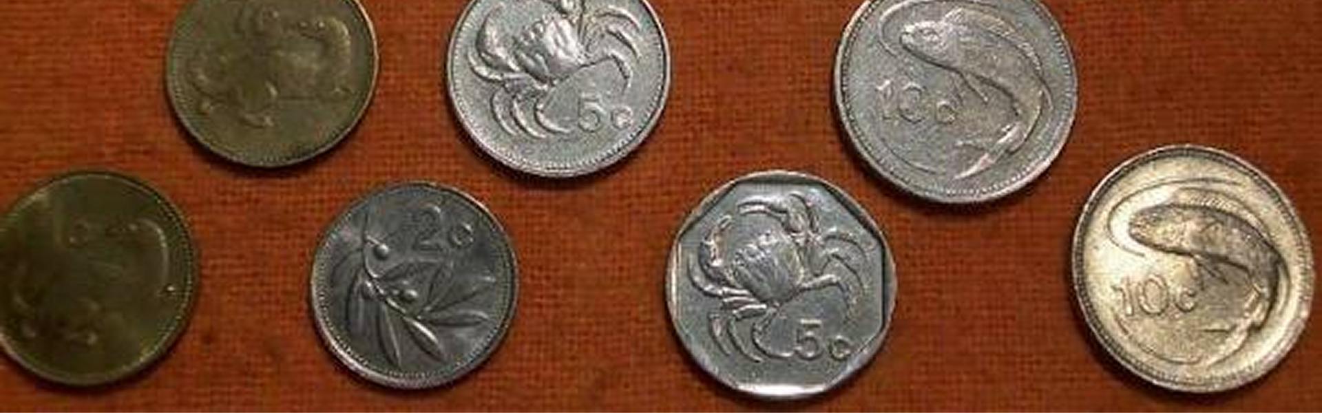Six Maltese Lira coins on a red cloth: two 1c weasel coins, a 2c olive-branch coin, two 5c crab coins (round and heptagonal editions), and two 10c lampuka fish coins.