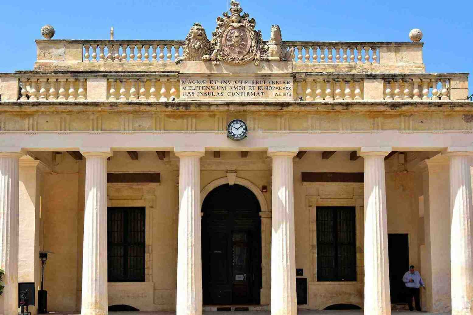 Facade of the Main Guard building in Valletta, Malta, featuring classical columns, a British Royal Coat of Arms, and a Latin inscription dated 1814