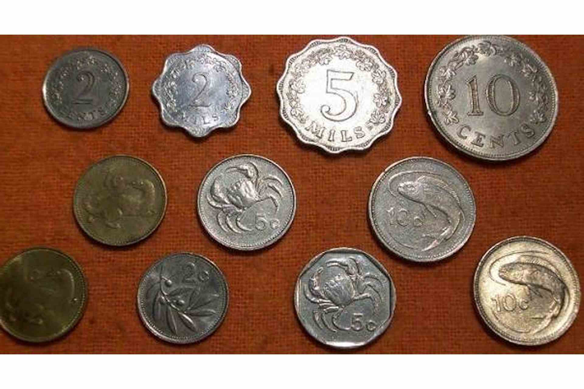 Collection of old Maltese coins on a red cloth, including pre-decimal mils and cents pieces and Lira-era coins depicting a weasel, crab, and lampuka fish.