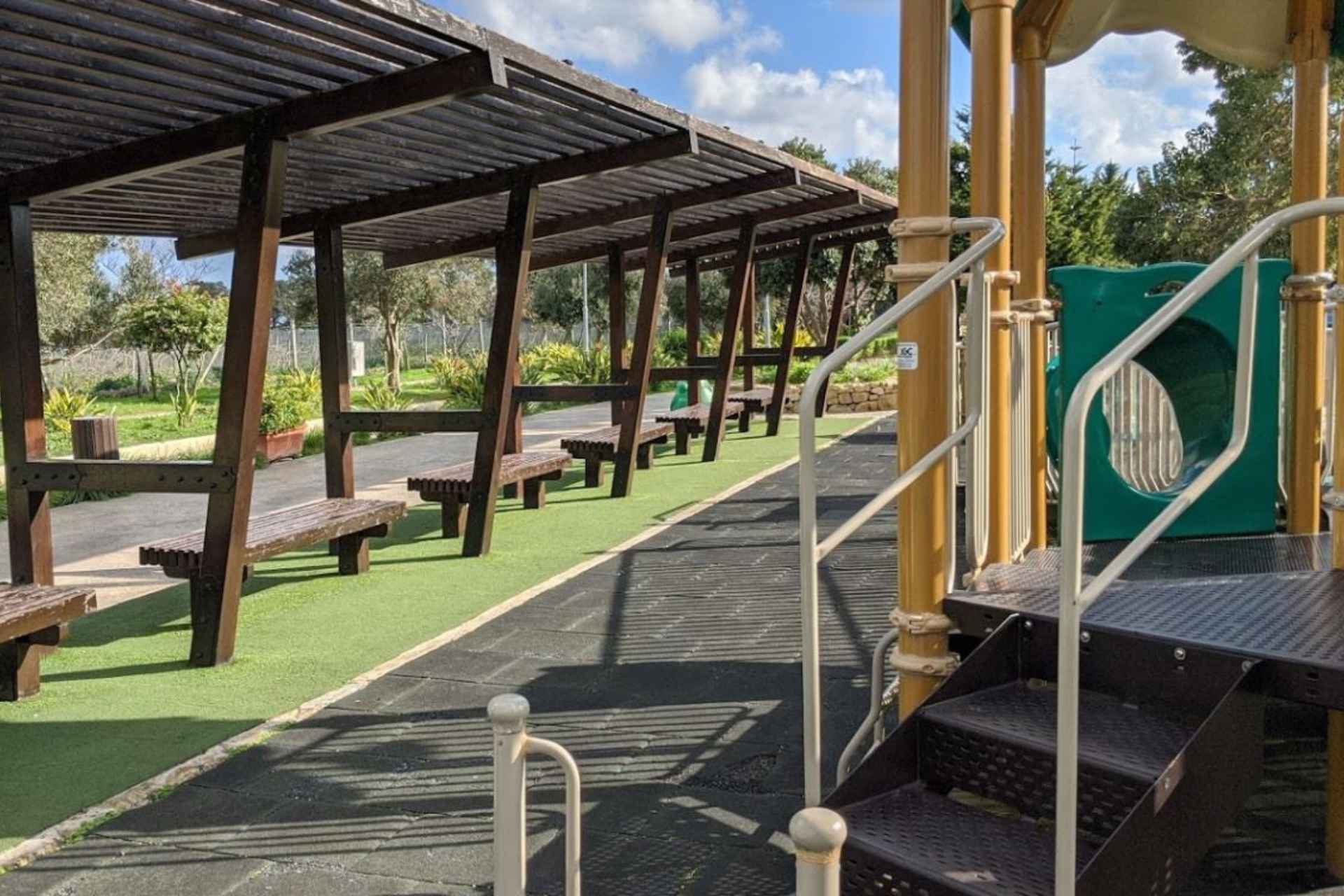 a row of wooden sheltered benches facing a playground