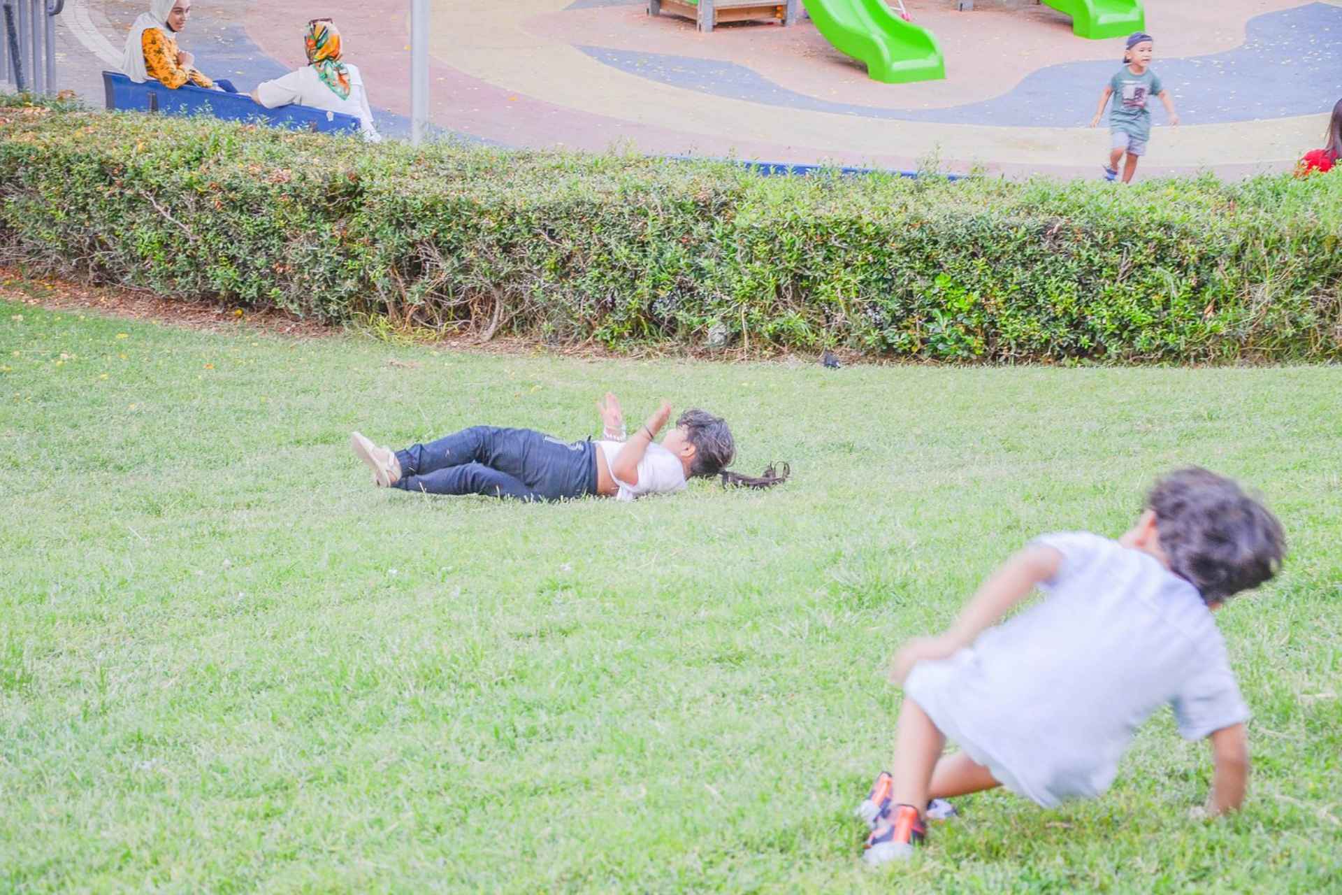 two kids rolling down a green slope