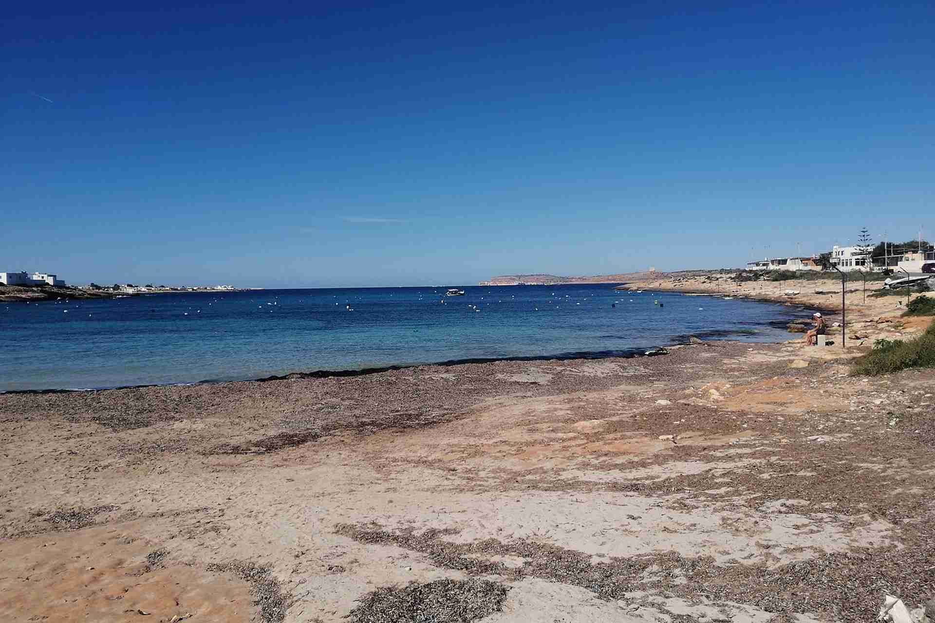 White Tower Bay in Malta, showing a sandy and rocky shoreline with clear blue water and a wide view of the bay under a clear sky